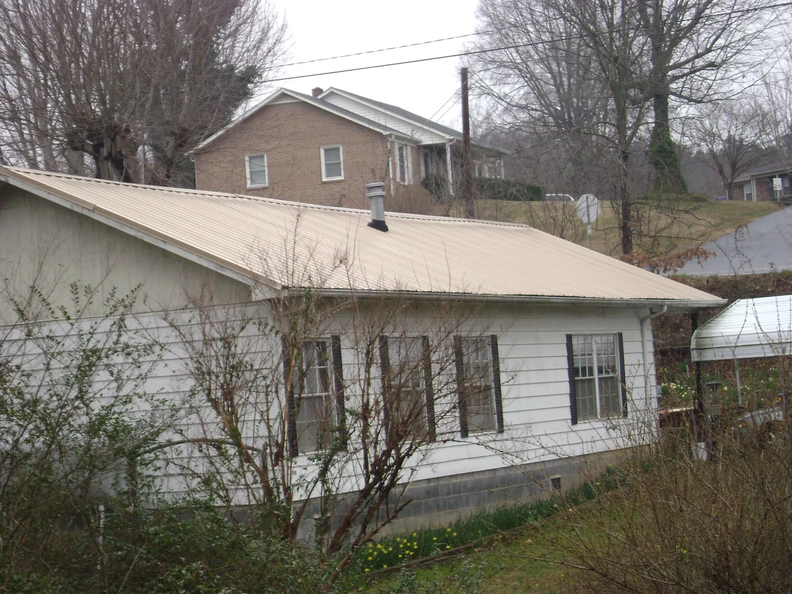 Tan metal roof on a white sided house set into a hillside — Commercial Roofing by Roofing Brothers in Silver Lake
